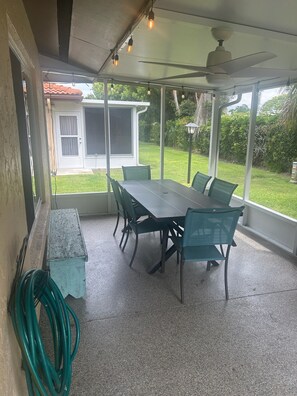 A covered patio area with a table and chairs, a ceiling fan, and a view of a house and garden.