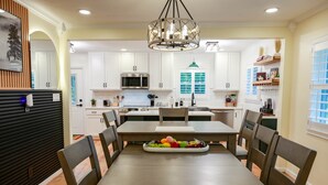 A modern kitchen with white cabinets, a central island, and a dining area with a wooden table and chairs.