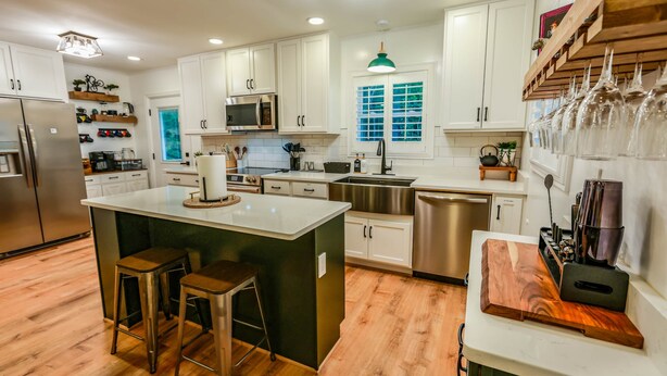 A modern kitchen with white cabinets, a central island with stools, stainless steel appliances, and a wooden countertop.