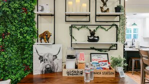 A snack station with a wooden sign, snacks, and water bottles. Shelves above display various items including candles, a bird sculpture, and a potted plant.