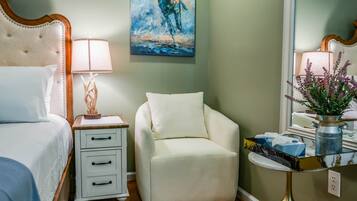 A bedroom with a bed, nightstand, chair, and bedside table with a lamp and decorative items.
