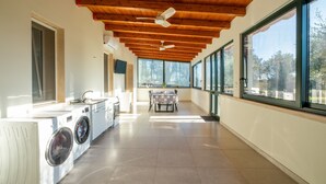 Un área de lavandería con ventiladores de techo, una mesa con sillas y ventanas grandes.
