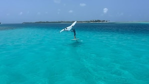 A person windsurfing in clear turquoise waters with a distant island in the background.