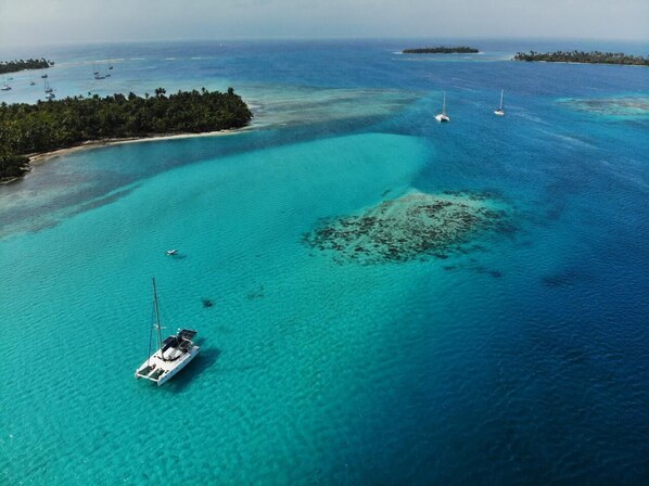 An aerial view of a turquoise sea with a small island and a boat.