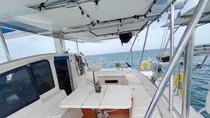 A boat's deck with a white cushioned seating area, a small table with a pineapple, and a view of the sea.