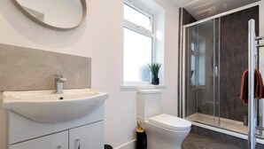 A modern bathroom with a white sink, toilet, and glass shower enclosure. - 4 Bedroom Apartment Central Redcar (Redcar and Cleveland)