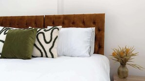 A bed with a tufted headboard, white bedding, and three pillows in different colors. - 4 Bedroom Apartment Central Redcar (Redcar and Cleveland)