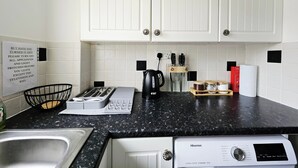 Een moderne keuken met witte kasten, een zwart granieten aanrecht, een koffiezetapparaat, een broodrooster en een Hisense stoomstrijkijzer.