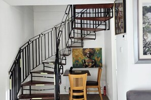 A spiral staircase with a black metal railing leading to a dining area with two wooden chairs and a table.