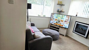 Een woonkamer met een bank, een loungestoel, een televisie en een open haard.