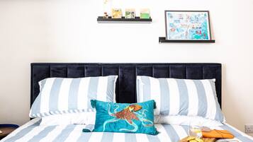 Una cama con ropa de cama a rayas, un cojín con diseño de pulpo, un mapa enmarcado en la pared y una pequeña estantería con objetos.