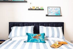 Ein Bett mit gestreifter Bettwäsche, ein Kissen mit einem Oktopus-Motiv, eine gerahmte Karte an der Wand und eine kleine Ablage mit Gegenständen.