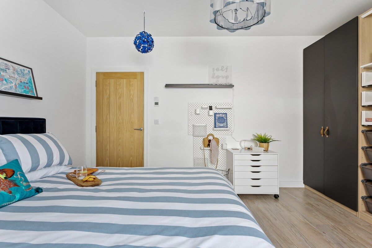Une chambre à coucher comprenant un lit, une commode, une armoire, une étagère fixée au mur et un luminaire suspendu.
