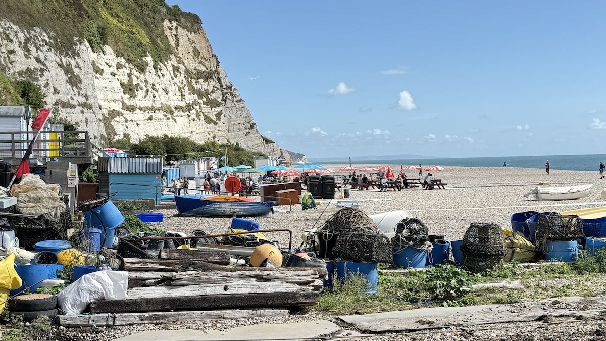 A beach with boats and fishing equipment, a rocky cliff, and umbrellas.