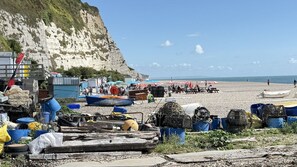 Une plage avec des bateaux et du matériel de pêche, une falaise rocheuse et des parasols.