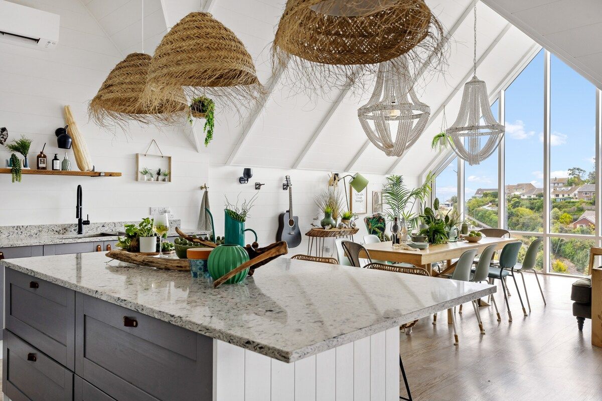 A modern kitchen with a large island, pendant lights, and a view of the surrounding landscape.