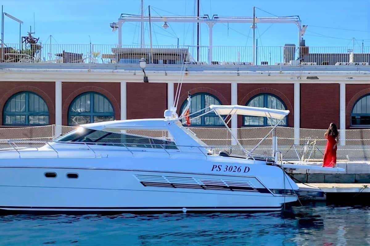 En vit lyxyacht låg förtöjd vid en småbåtshamn, med en byggnad i tegel som bakgrund.