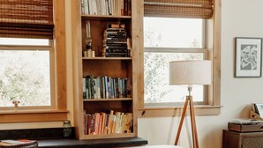 A kitchen with a large island, wooden bookshelves, a dining table, and a window with blinds. - Backroad Cabin • cozy, private retreat, fireplace, backyard with fire pit and string lights. (Emigrant)