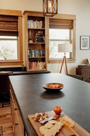 Una cocina con una isla grande, estanterías de madera, una mesa de comedor y una ventana con persianas.