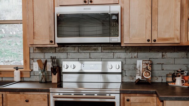 A kitchen with wooden cabinets, a microwave, a stove, and a coffee maker. - Backroad Cabin • cozy, private retreat, fireplace, backyard with fire pit and string lights. (Emigrant)