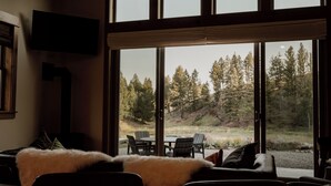 A living room with a large window, a flat-screen TV, and a fireplace. - Backroad Cabin • cozy, private retreat, fireplace, backyard with fire pit and string lights. (Emigrant)