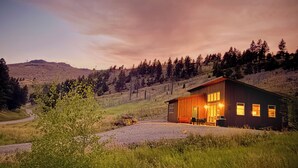 Una baita di legno con un portico, immersa in un paesaggio erboso e alberato.
