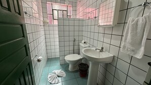 Une petite salle de bain avec des carreaux blancs, des toilettes, un lavabo et une fenêtre ornée de rideaux roses.