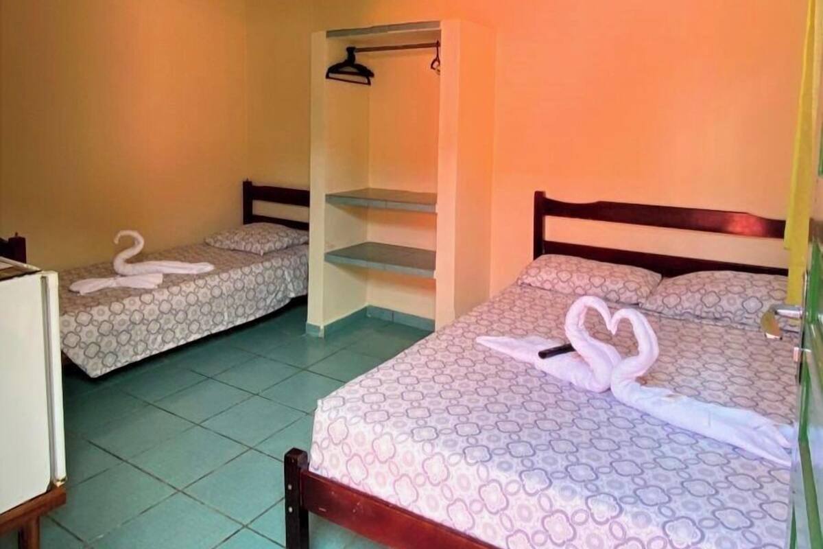 A hotel room with two beds, each with a towel swan decoration, a ceiling fan, and a small shelf unit.