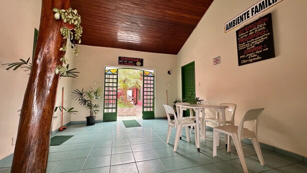 Un couloir avec un plafond en bois, une porte verte et une pancarte sur laquelle on peut lire « AMBIANCE FAMILIALE ». La pièce contient des chaises en plastique blanches et une petite table.