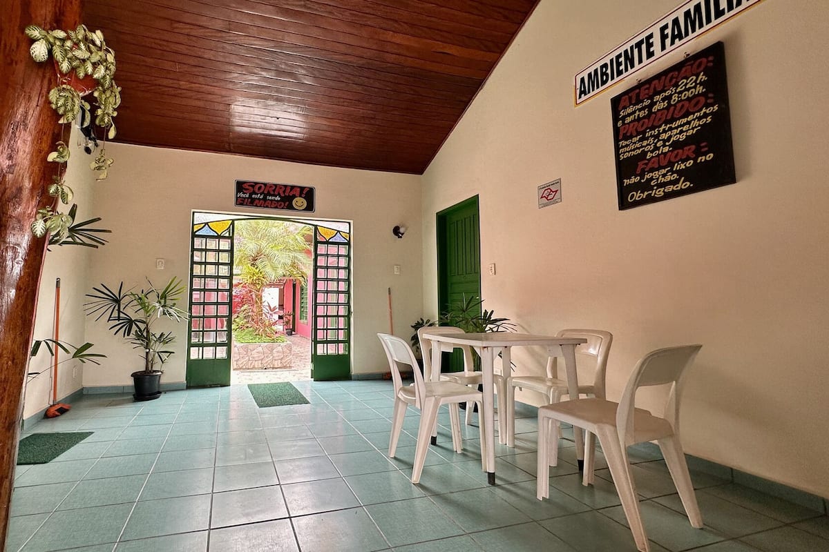 A hallway with a wooden ceiling, a green door, and a sign that reads "AMBIENTE FAMILIAR." There are white plastic chairs and a small table in the room.