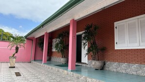 Un bâtiment à la façade en briques rouges, à l’extérieur rose et doté d’un porche abrité orné de plantes en pot.