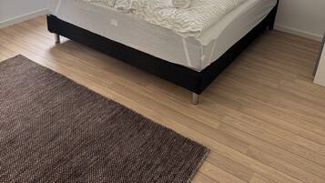 A modern bedroom with a black headboard, two beds, a window, a lamp, and a brown rug.
