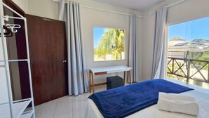 Un dormitorio con cama, escritorio y ventana con vistas a un edificio y palmeras.