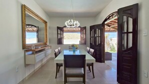 Un comedor con una mesa larga, sillas y una araña. Hay puertas abiertas que dan a un espacio exterior.