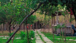 Un chemin de pierres qui traverse un jardin planté d’arbres et mène à une structure en bois.