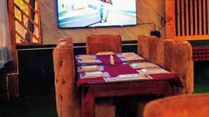 Un coin repas avec une table dressée pour deux personnes, un téléviseur fixé au mur et des chaises en bois.