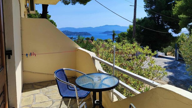 A balcony with a table and chair, overlooking a scenic view of the sea and hills.