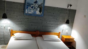 A room with two beds, a painting on the wall, and two pendant lights.