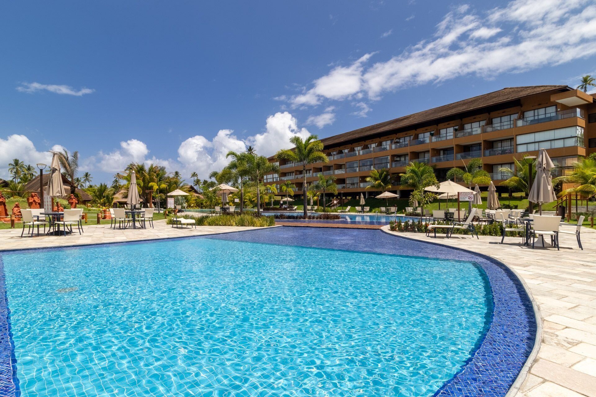 A hotel with a large swimming pool, outdoor seating, and palm trees.