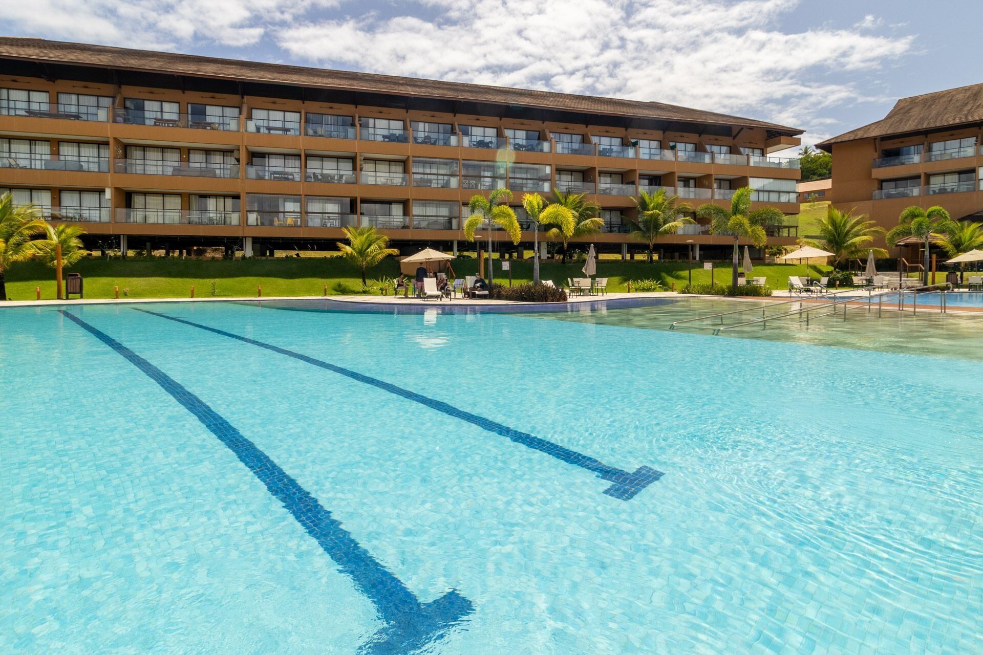 Un hotel con una gran piscina, varios balcones y palmeras.