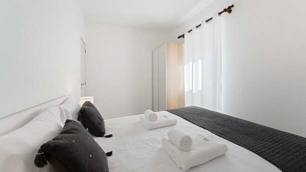 A modern hotel room with a bed, two pillows, a bedside table with a lamp, a mirror, and a window with curtains. - GuestReady - Rosemary's lovely home with a garden (Porto)