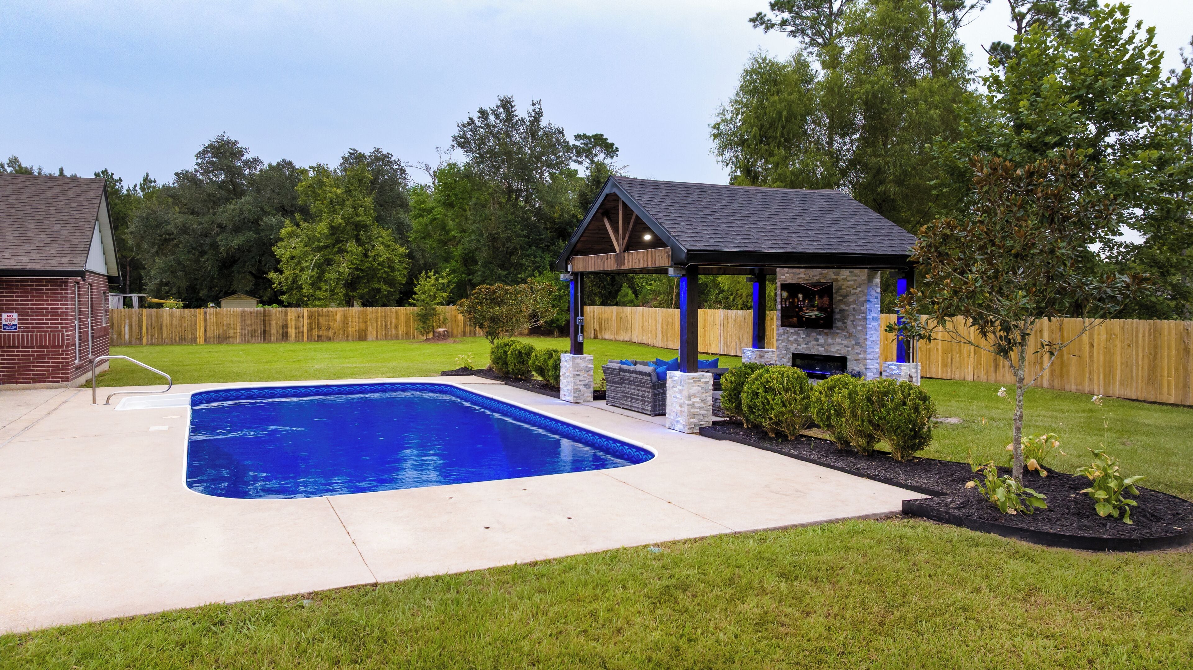 A backyard with a swimming pool, a covered patio, and a brick house.