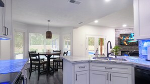 Una cocina moderna con armarios blancos, encimera de granito y comedor con mesa y sillas.