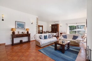 A living room with two sofas, a coffee table, a console table with lamps, and a dining area in the background.