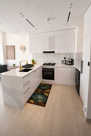 A modern kitchen with white cabinetry, a marble countertop, a built-in oven, a coffee maker, and a washing machine.