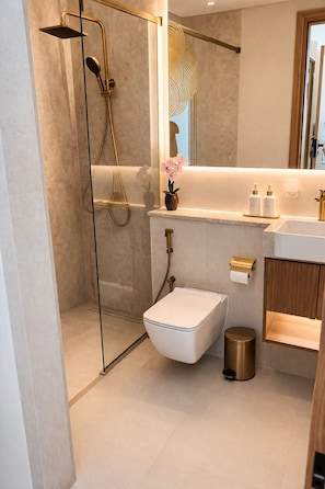 A modern bathroom with a glass-enclosed shower, a white toilet, a sink with gold fixtures, and a mirror above the vanity.
