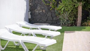 Three white lounge chairs with a stone wall and greenery in the background.