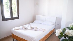 A single bed with a wooden frame and white bedding, a white headboard, and a window with blinds.