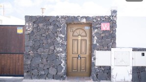 A stone wall with a brown door, a sign with a 'W' logo, and a metal gate.