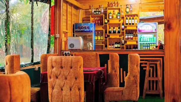 Eine Bar mit Holzkleidern, einer Klimaanlage mit dem Schriftzug 'BOSS' und Regalen voller verschiedener Flaschen.